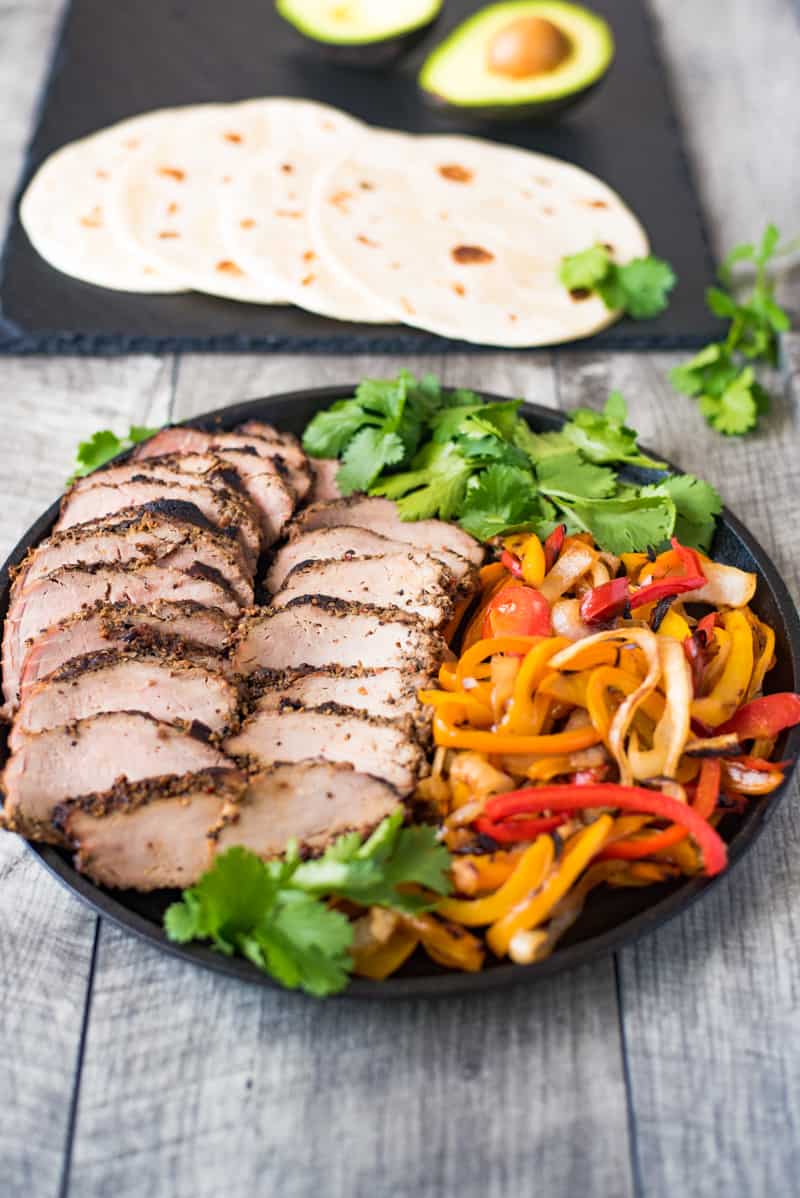 Grilled pork tenderloin fajitas are a quick and easy way to get a summer meal served in under 30 minutes. Marinated pork tenderloin is grilled along with onions and peppers. The pork is sliced then all are served on warm tortillas garnished with fresh avocado and cilantro.