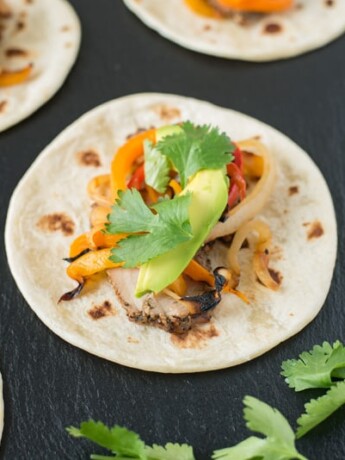 Grilled pork tenderloin fajitas are a quick and easy way to get a summer meal served in under 30 minutes. Marinated pork tenderloin is grilled along with onions and peppers. The pork is sliced then all are served on warm tortillas garnished with fresh avocado and cilantro.