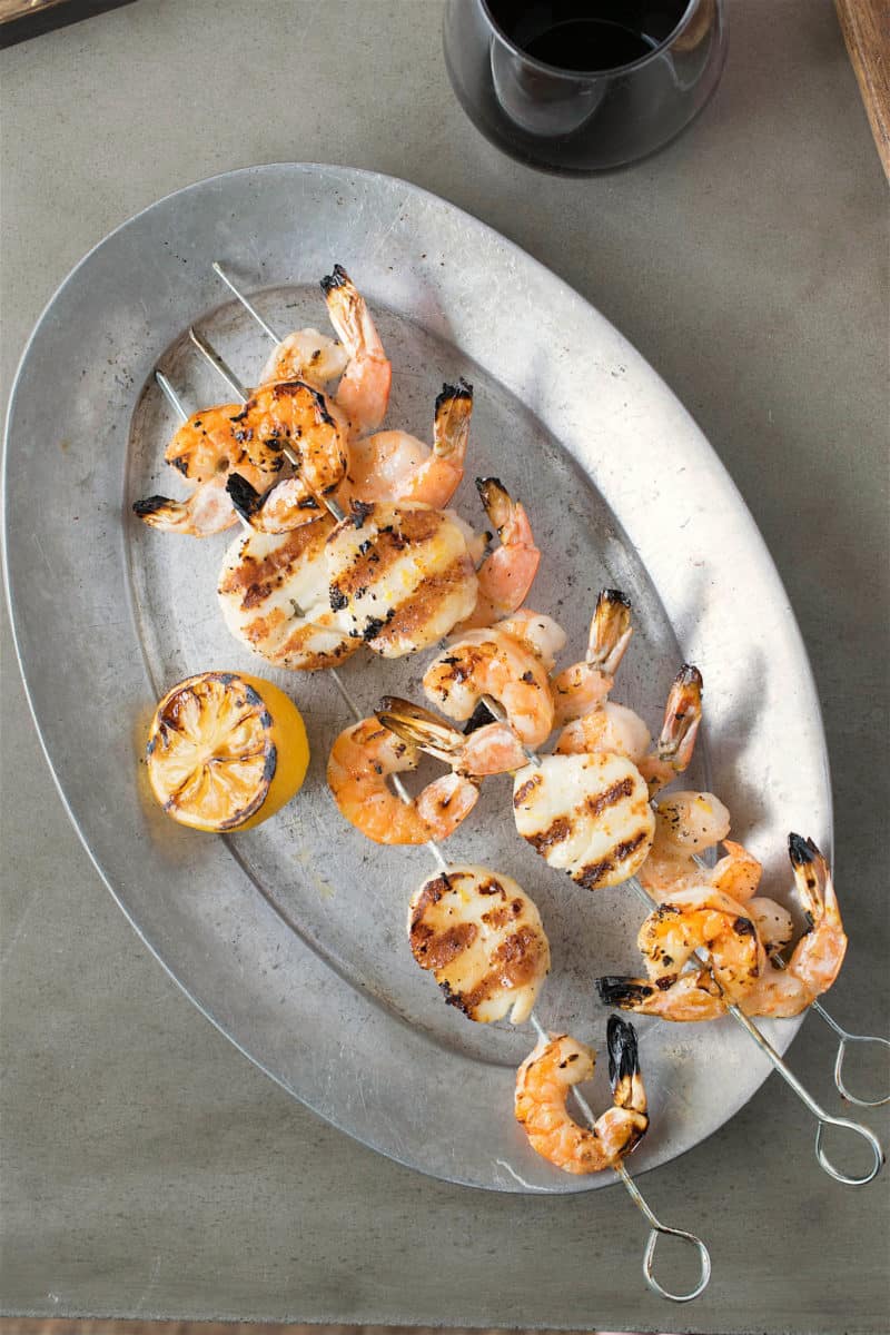 Grilled shrimp and scallop kebobs from overhead on a pewter plate with grilled lemon