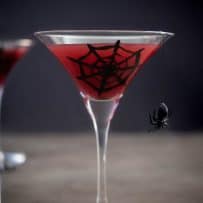 A spooky Halloween drink of a blood orange martini with a spider web and spider on the glass