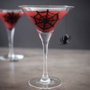 2 martini stemmed glasses with blood orange juice decorated with a spider web and spider