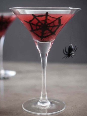 2 martini stemmed glasses with blood orange juice decorated with a spider web and spider