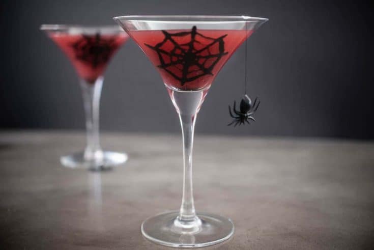 2 martini stemmed glasses with blood orange juice decorated with a spider web and spider