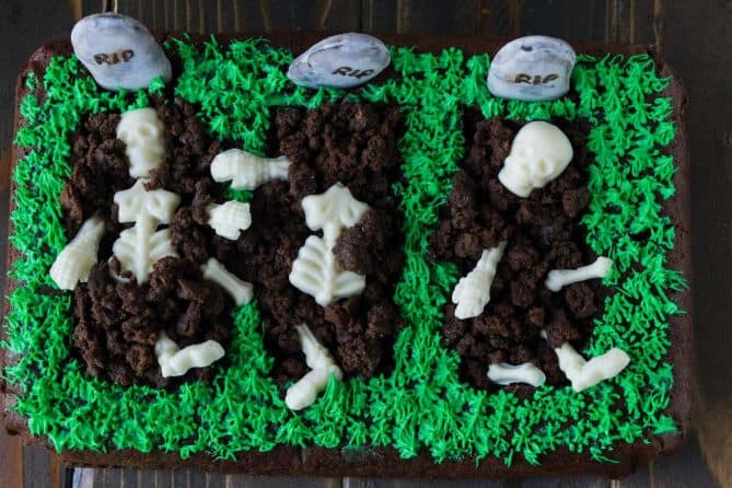 3 graves cut out of a brownie with white chocolate skeletons buried