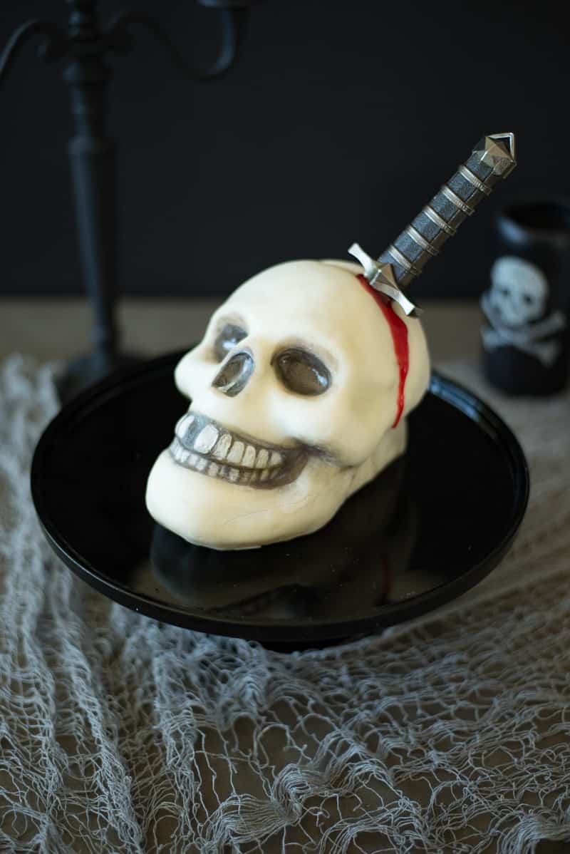 A Halloween skull and dagger cake on a black cake stand