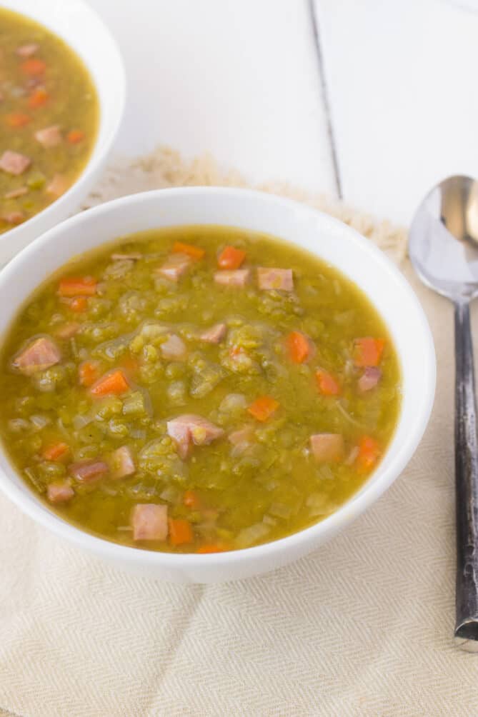 A bowl of green pea soup with ham and carrots
