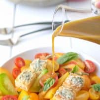 Pouring vinaigrette over a colorful heirloom tomato salad