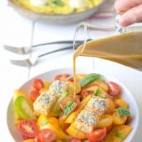 Pouring dressing over colorful heirloom tomatoes with fresh basil and croutons