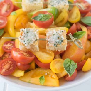 2 Parmesan basil croutons on a skewer on top of tomato salad