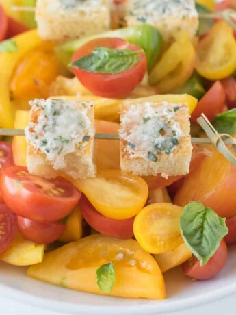 2 Parmesan basil croutons on a skewer on top of tomato salad