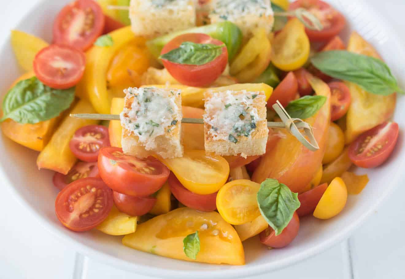2 Parmesan basil croutons on a skewer on top of tomato salad