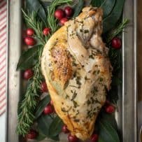 An overhead view of a herb roasted turkey breast on a sliver tray garnished with herbs and cranberries