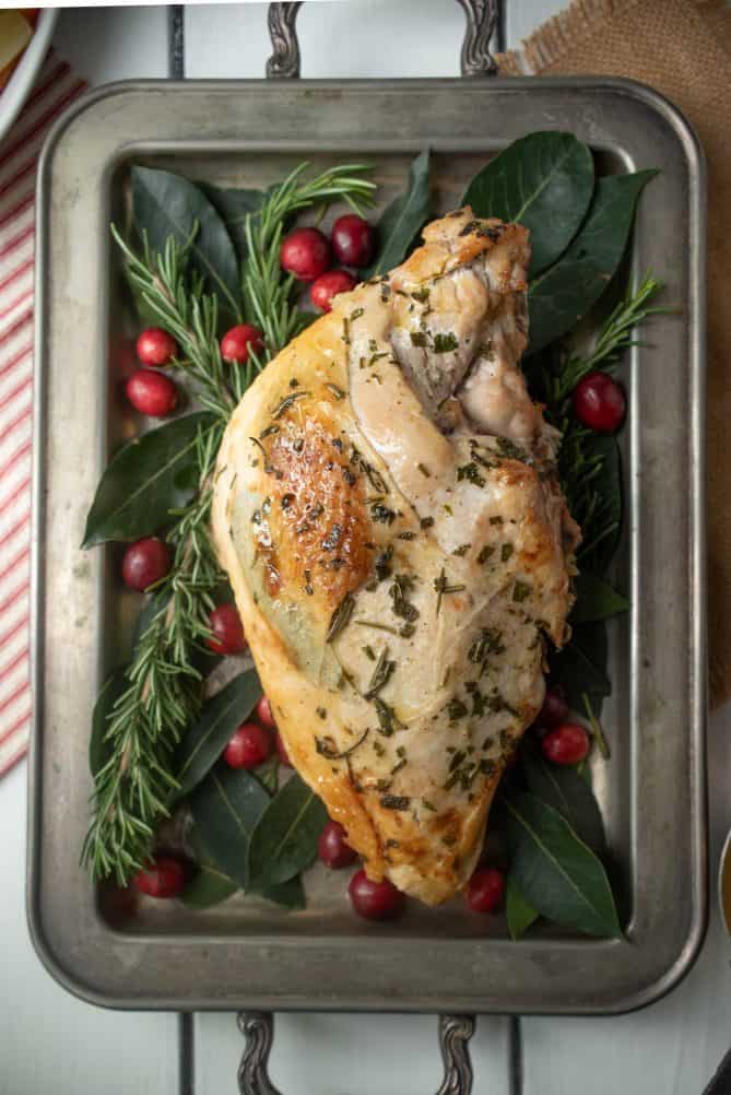 An overhead view of a herb roasted turkey breast on a sliver tray garnished with herbs and cranberries