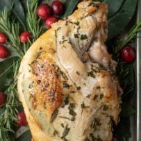 Browned, crisp skin on a turkey breast with fresh herbs on a bed of fresh herbs, leaves and fresh cranberries