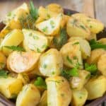 A closeup of potato wedges in potato salad with fresh herbs