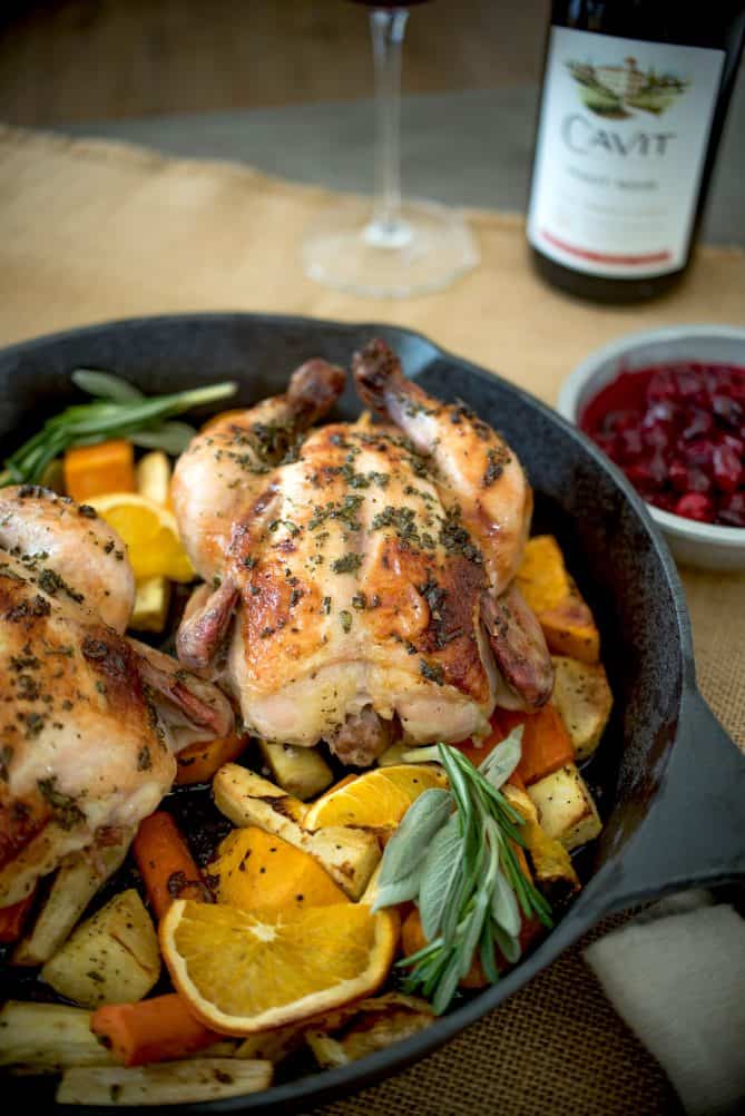 A closeup showing the Cornish hen coated in herbs garnished with orange slices and fresh sage
