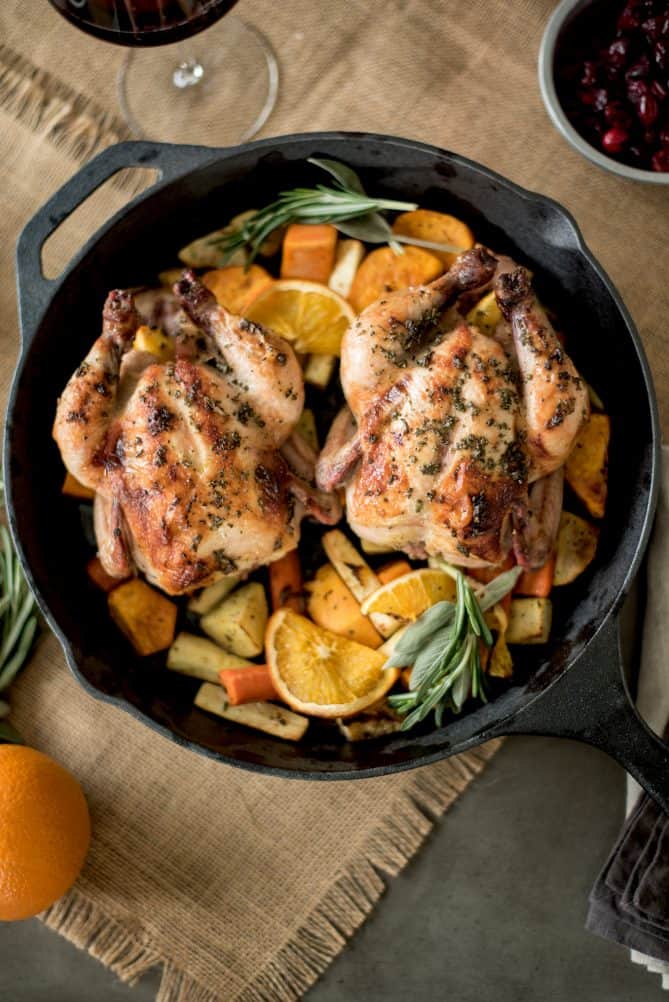 An overhead view of 2 Cornish hens in a cast iron skillet with vegetables under the hens