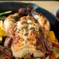 A whole Cornish hen coated in fresh herbs on a bed of vegetables that were roasted in a cast iron pan