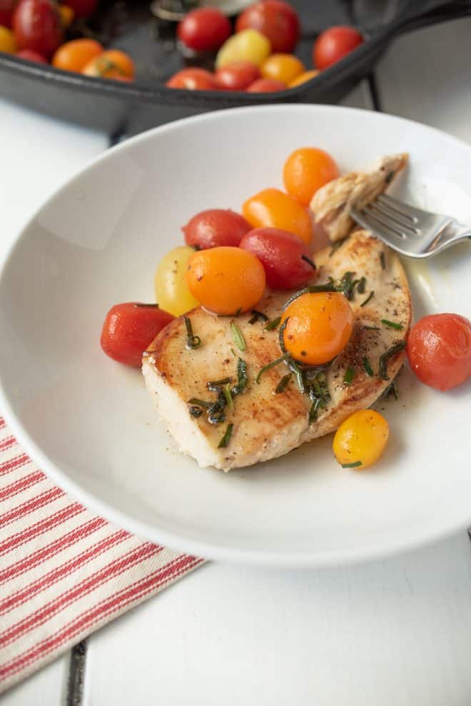 A chicken breast with herbed brown butter and tomatoes on a white plate