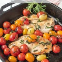 Vibrant red orange and yellow cherry tomatoes in a pan with chicken breasts and herbs