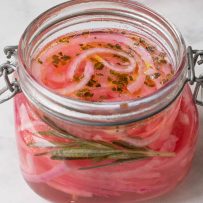 A sealable jar with red onions pickling in vinegar and herbs