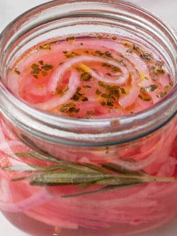A sealable jar with red onions pickling in vinegar and herbs