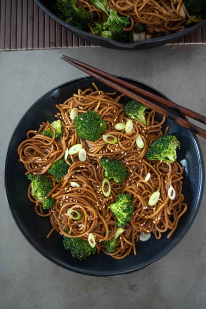 Noodles and broccoli in a black bowl with chopsticks