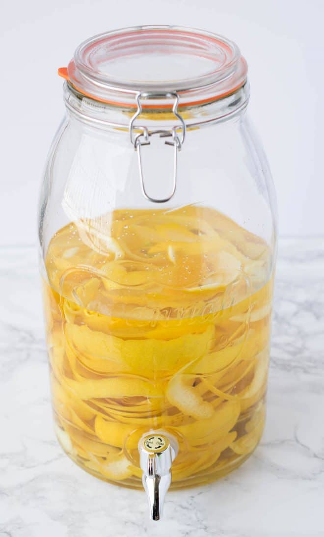 A large drink dispenser with lemon rinds and alcohol to make limoncello