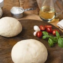 Yeast free pizza dough on a pizza board with tomatoes, basil, garlic and oil