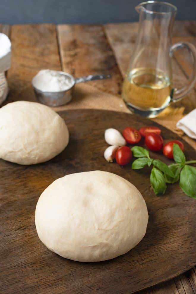Yeast free pizza dough on a pizza board with tomatoes, basil, garlic and oil