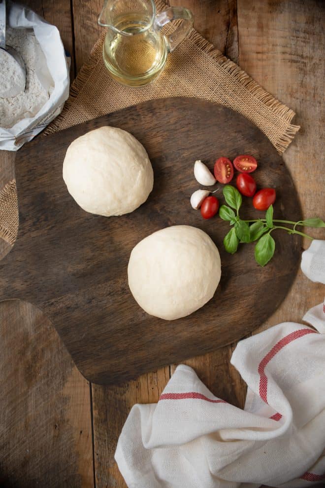 2 pizza dough balls on a board with tomatoes and basil
