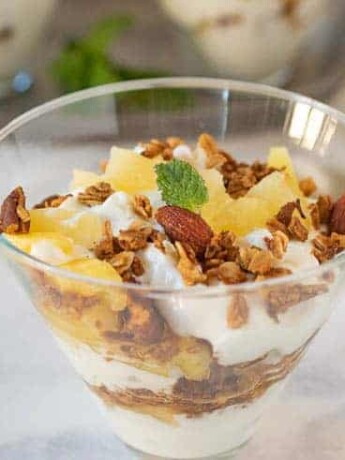 Layers of yogurt with granola and pineapple in a glass bowl