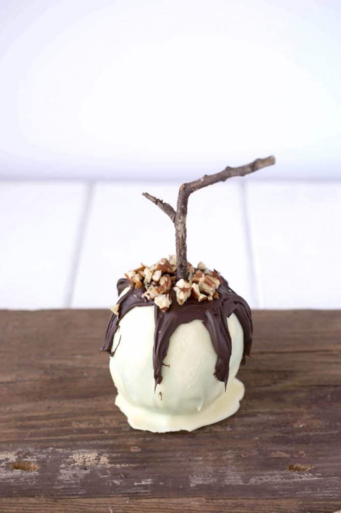 An apple coated in white chocolate with dark chocolate drizzled over and chopped pecans