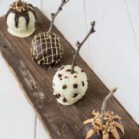 White and dark chocolate coated apples with real sticks inserted for handles on a distressed board
