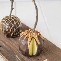 2 chocolate apples decorated with caramel and nuts on a board