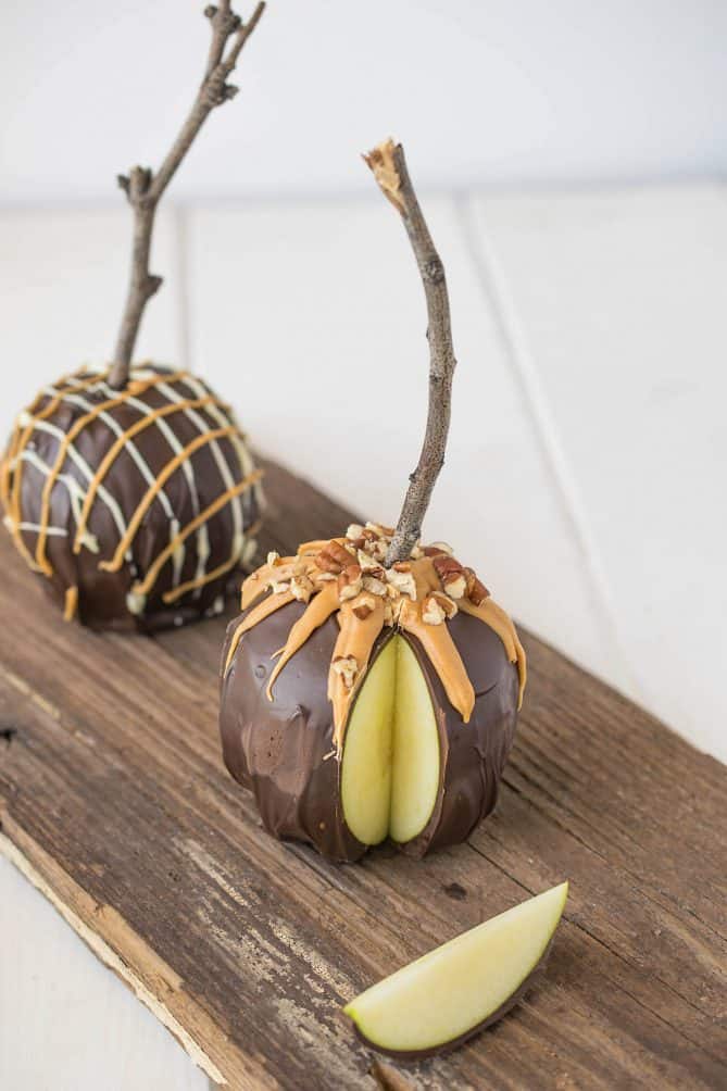 2 chocolate apples decorated with caramel and nuts on a board