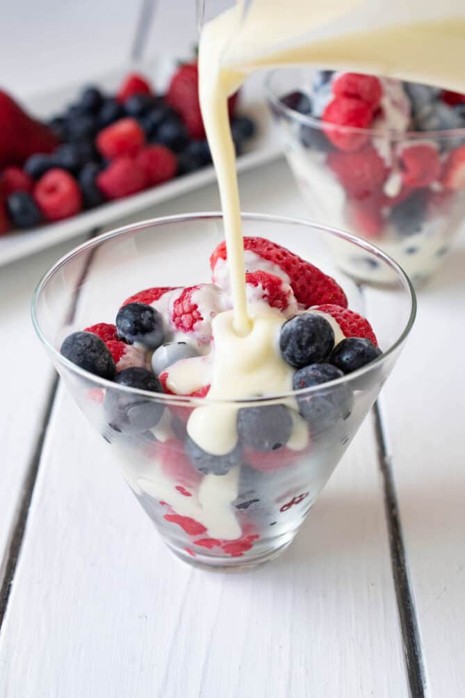 Frozen blueberries, strawberries and raspberries in a glass bowl with custard sauce being poured over