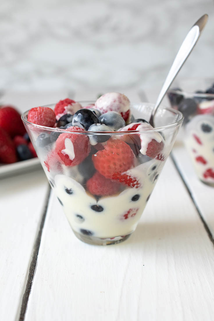 Custard and berries in a glass bowl with a spoon