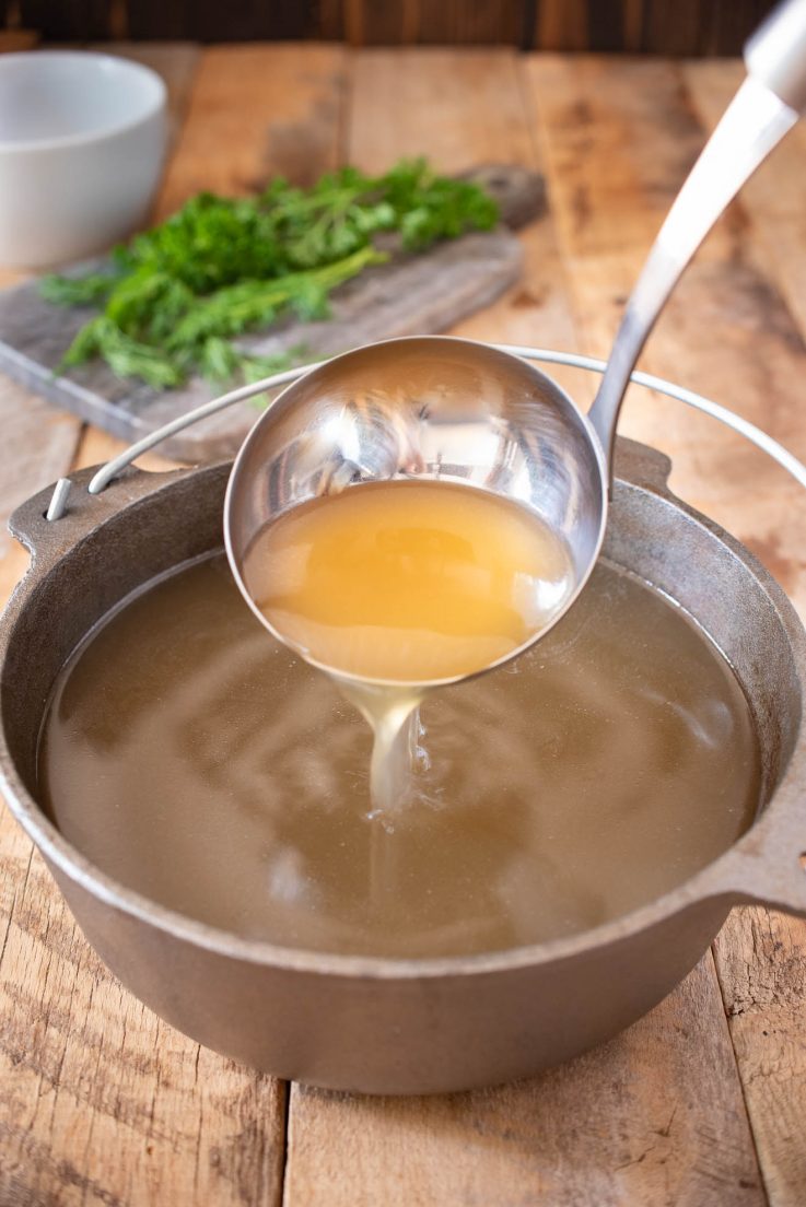A ladle of broth being poured in to a cast iron pan