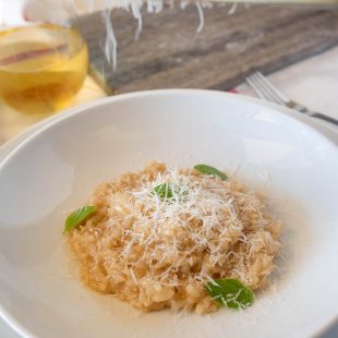 Grating Parmesan cheese onto a plate of risotto with fresh basil leaves
