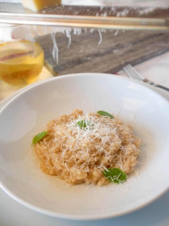 Grating Parmesan cheese onto a plate of risotto with fresh basil leaves