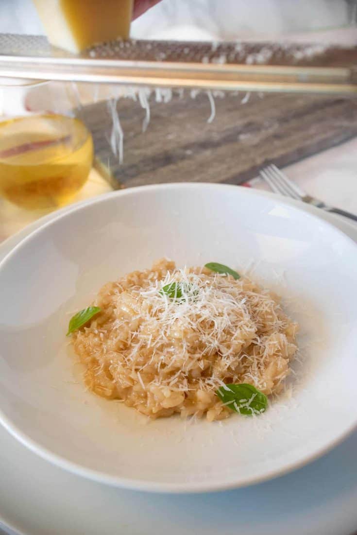 Grating Parmesan cheese onto a plate of risotto with fresh basil leaves