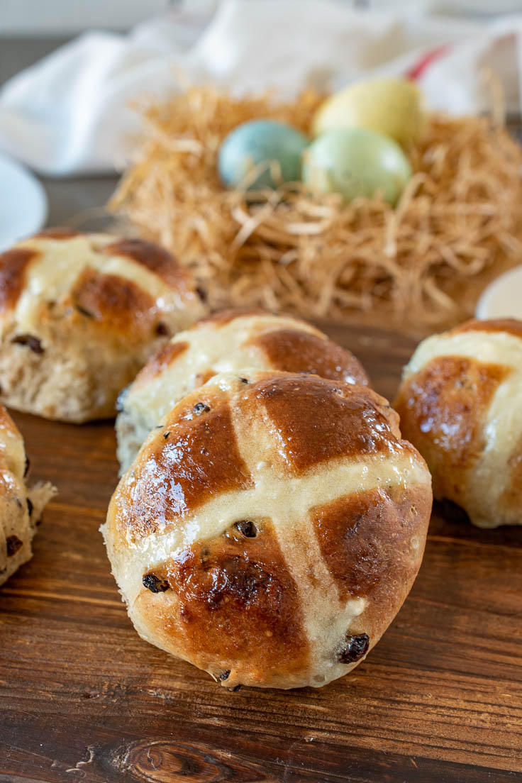 A closeup of a hot cross bun on a board with Easter eggs