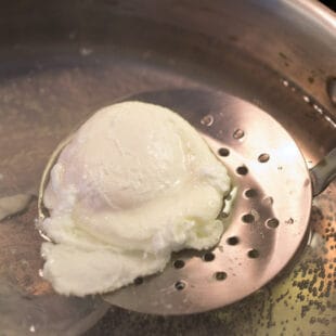 Using a slotted spoon to remove a poached egg
