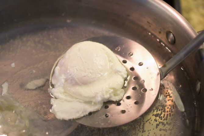 Using a slotted spoon to remove a poached egg