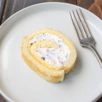 A slice of Ice Cream Swiss Roll Cake on a round white plate with a fork