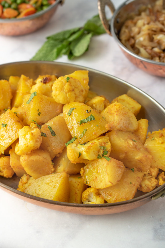 An oval serving dish full of Indian aloo gobi