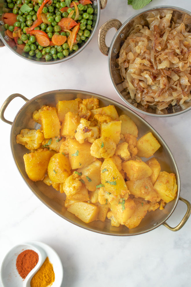 Indian aloo gobi from overhead with peas, curry caramelized onions in serving dishes