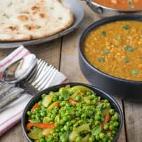 A bowl of peas and vegetables with dal, curry and naan bread