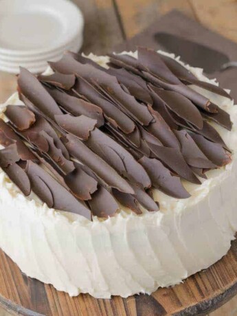 A buttercream frosted chocolate cake topped with chocolate shards on a cake stand